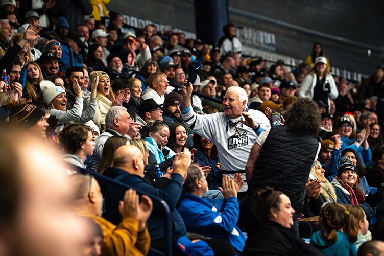An older man waves his hat to the crowd at a hockey game