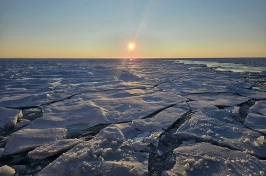 A frozen body of water with the sun low on the horizon